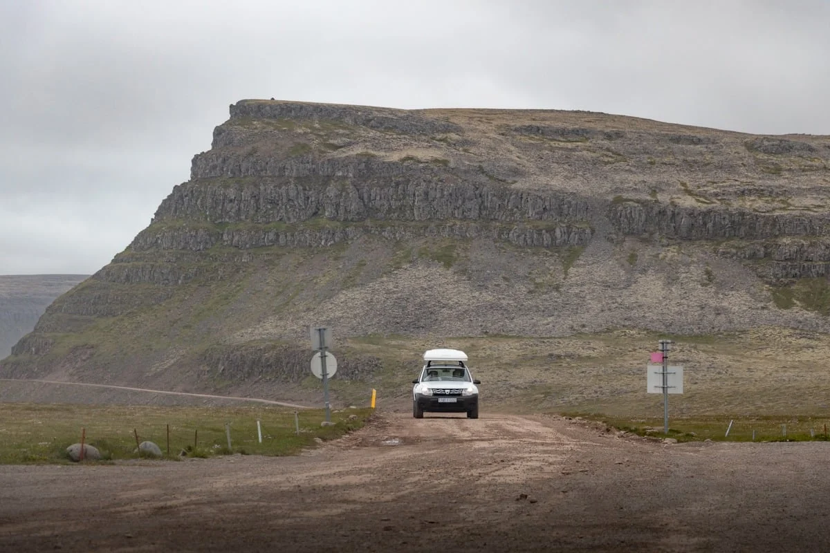 Un 4x4 blanc avec toit relevable sur une piste de gravier avec montagne en arrière plan