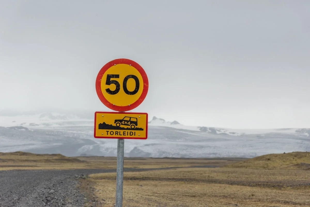 Panneau de limitation 50 km/h et piste 4x4 devant un glacier enneigé