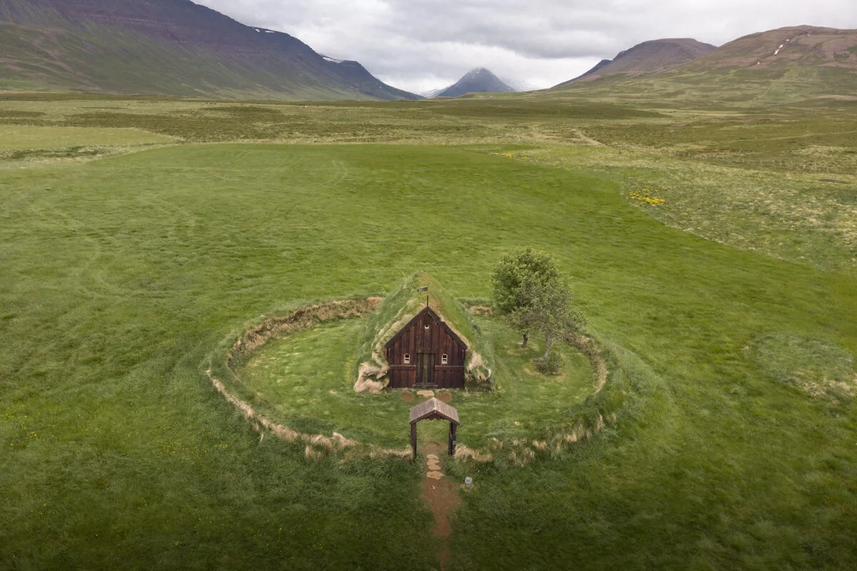 ancienne église en bois avec toit en gazon entourée d'un mur circulaire au milieu de verdure