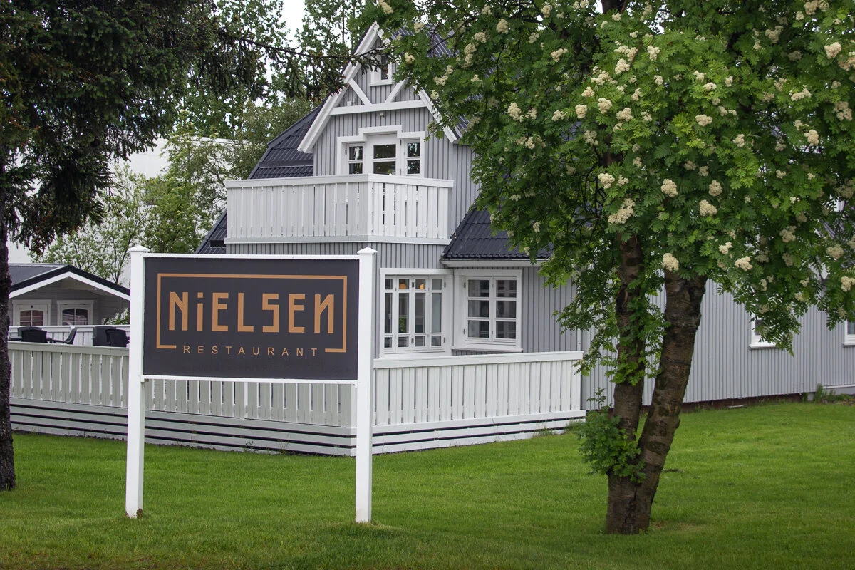 la façade du restaurant "Nielsen" derrière une pelouse et des arbres