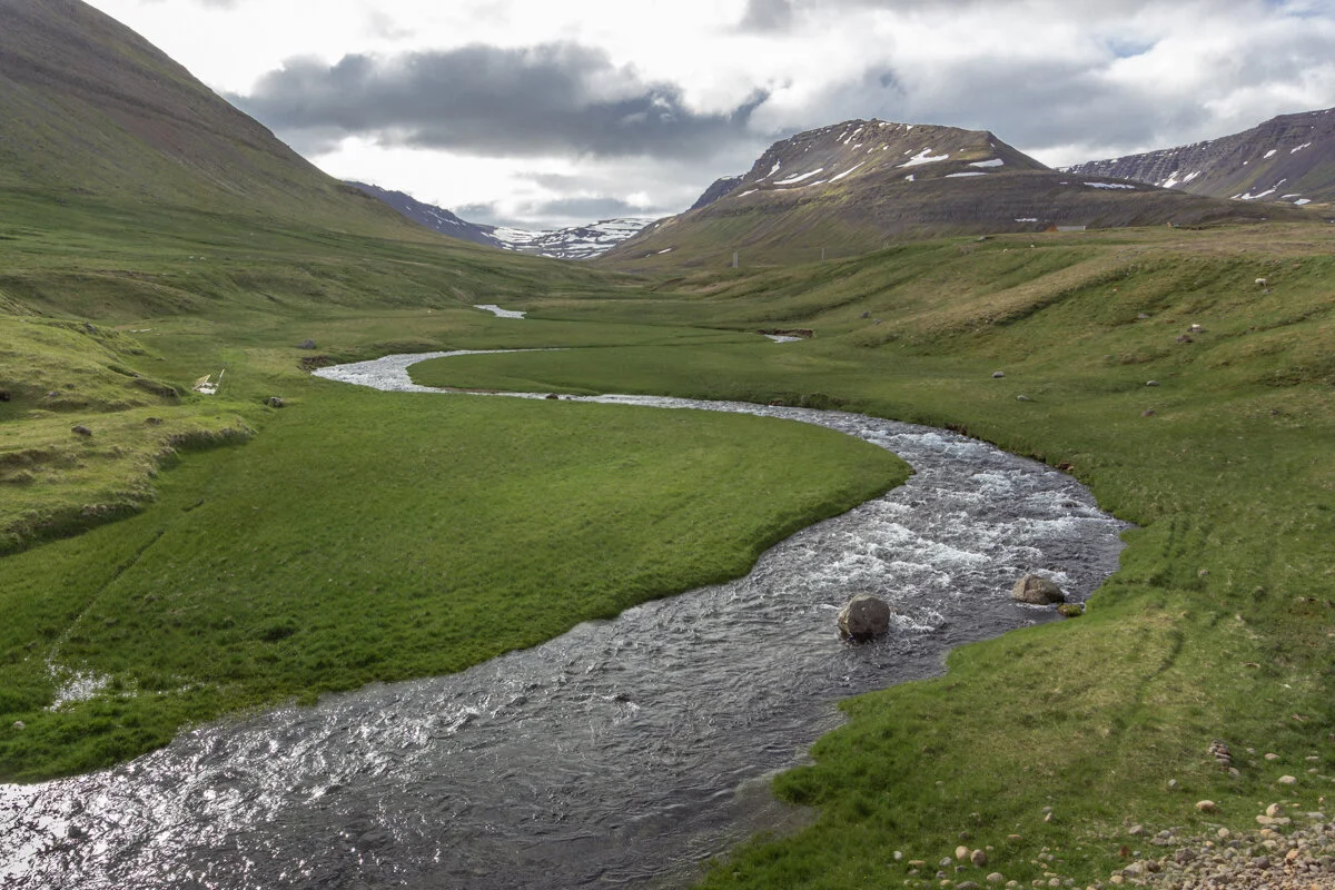 un cours d'eau serpente dans une vallée montagneuse verdoyante