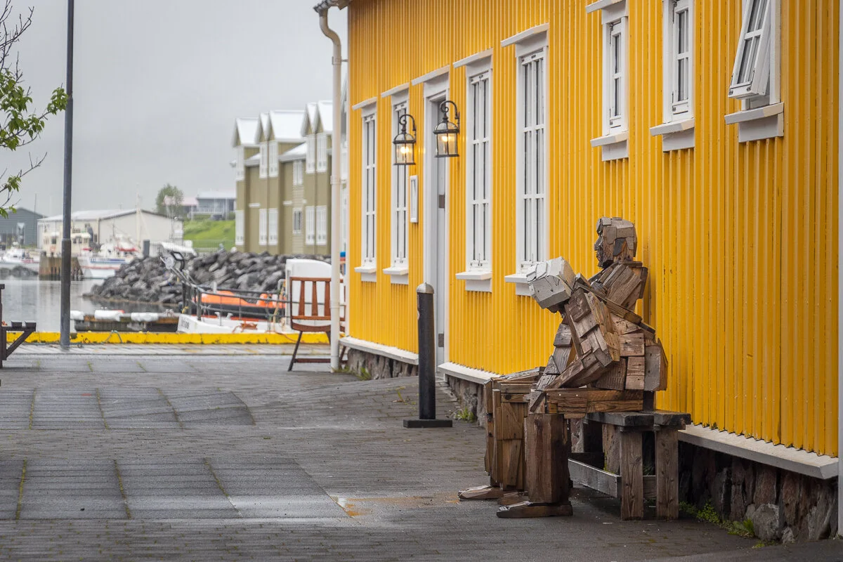 statue d'un personnage assis près d'une maison jaune