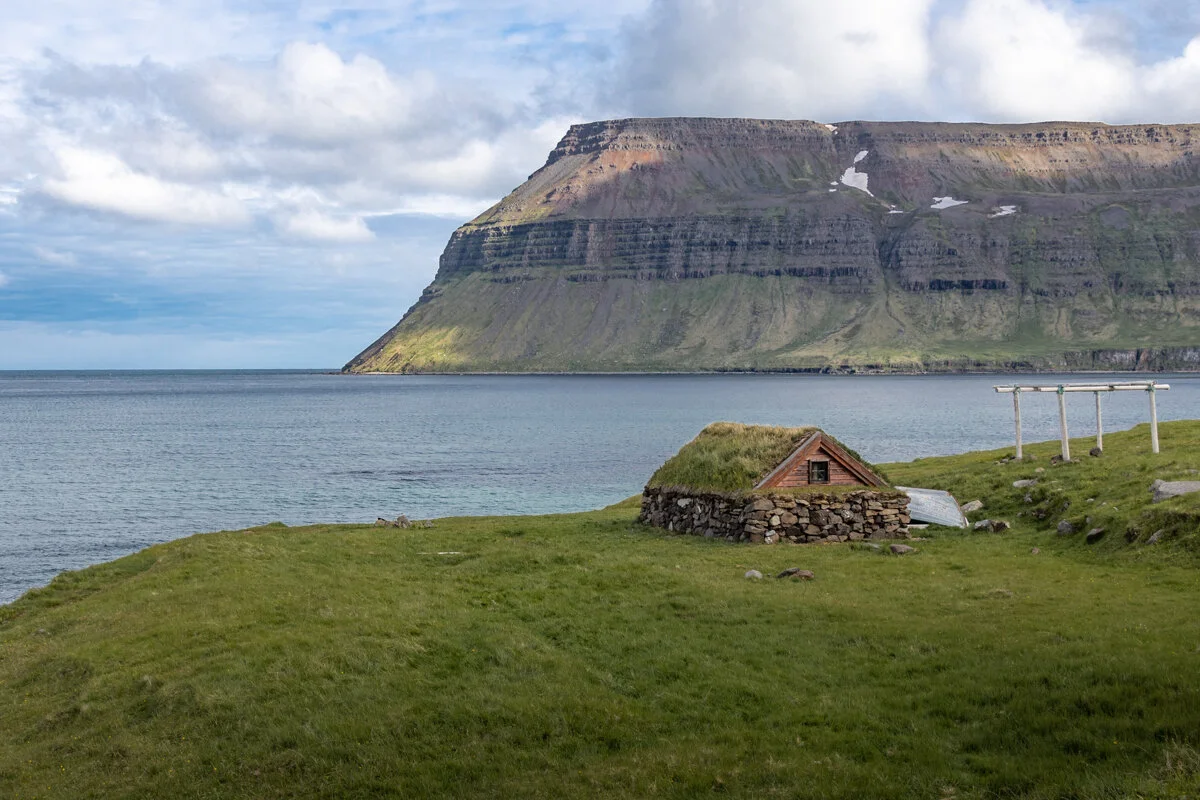 montagne avec falaises surplombant l'océan, avec une turfhouse au premier plan