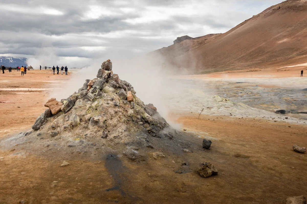 un geyser émet de la vapeur dans un paysage géothermique désertique