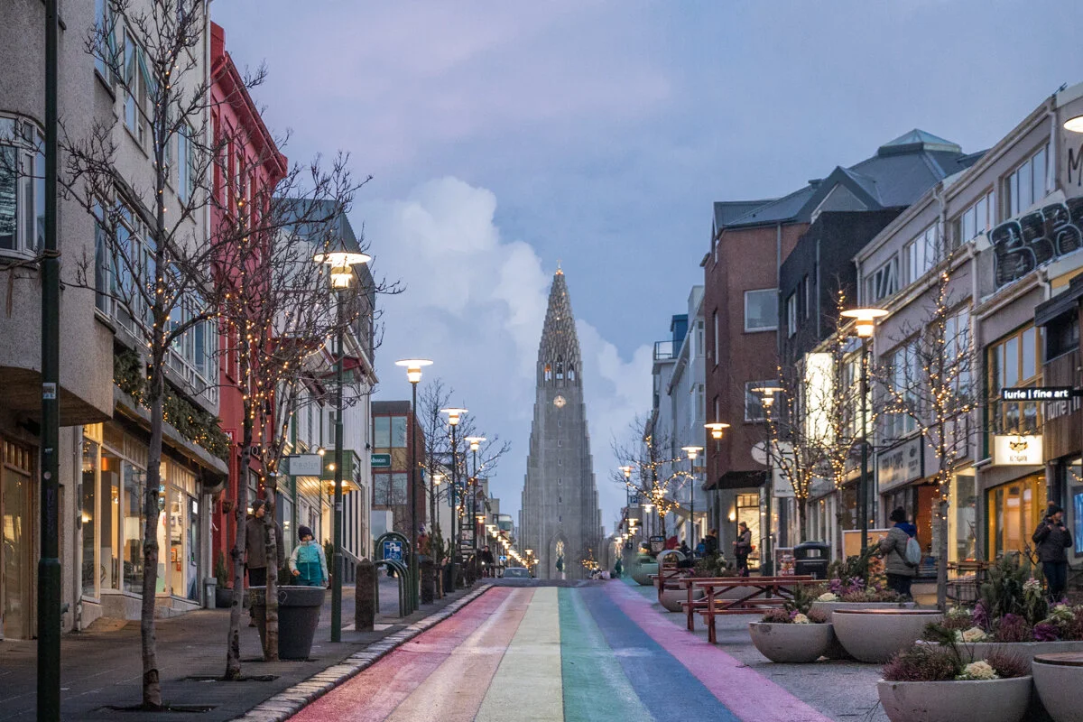 rue urbaine avec arc-en-ciel peint au sol, commerces, et église au fond