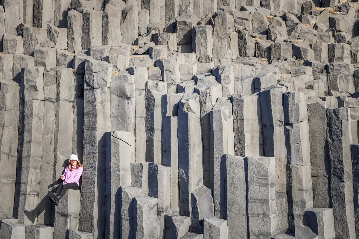 une personne assise sur une formation rocheuse de colonnes basaltiques