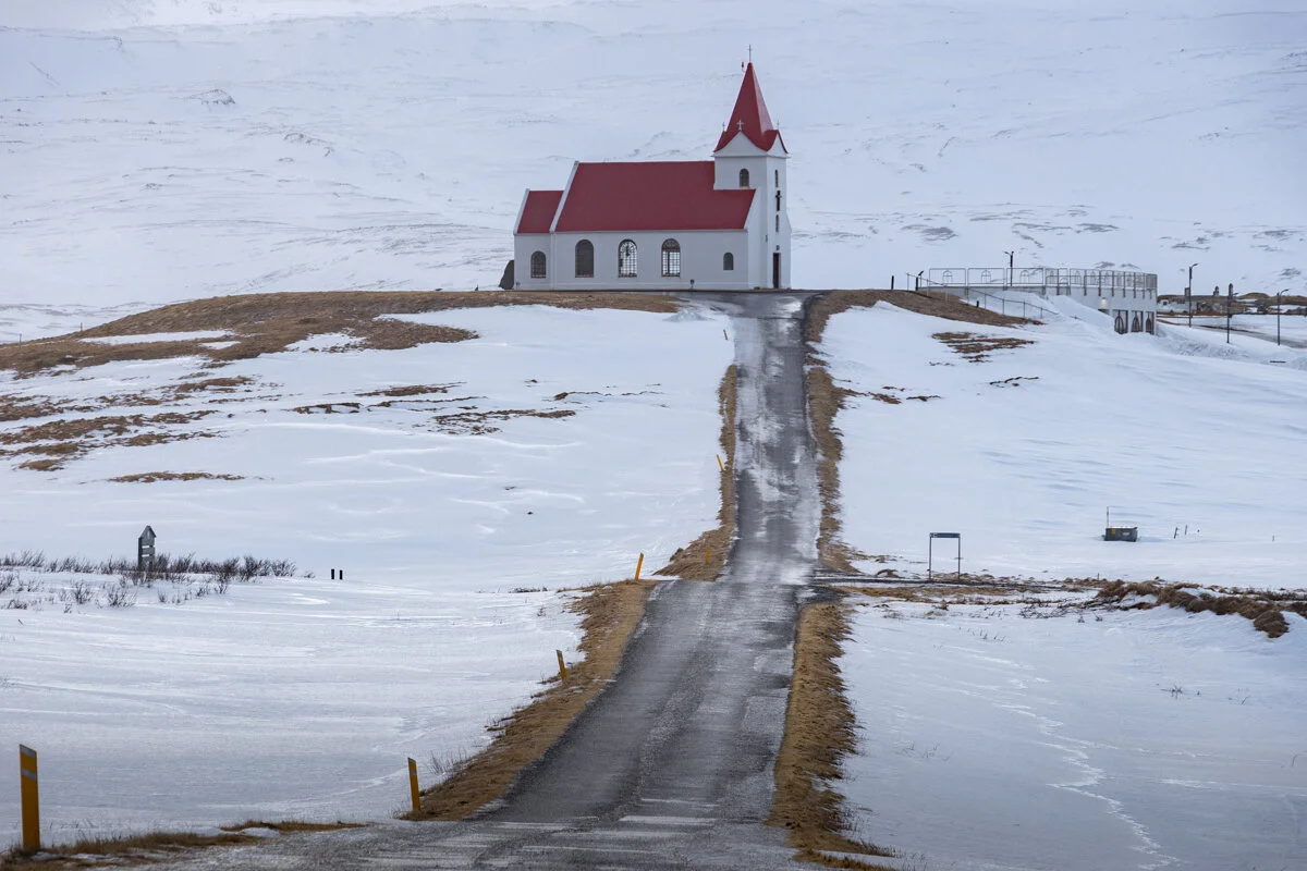 église rouge et blanche au bout d'une route gelée, bordée de neige