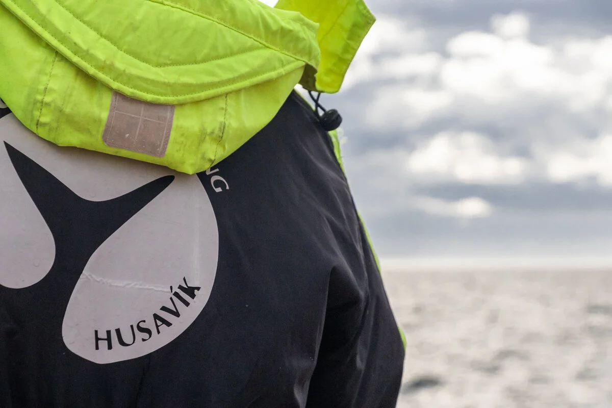 personne portant un coupe vent jaune et noir avec la mention "Husavik"