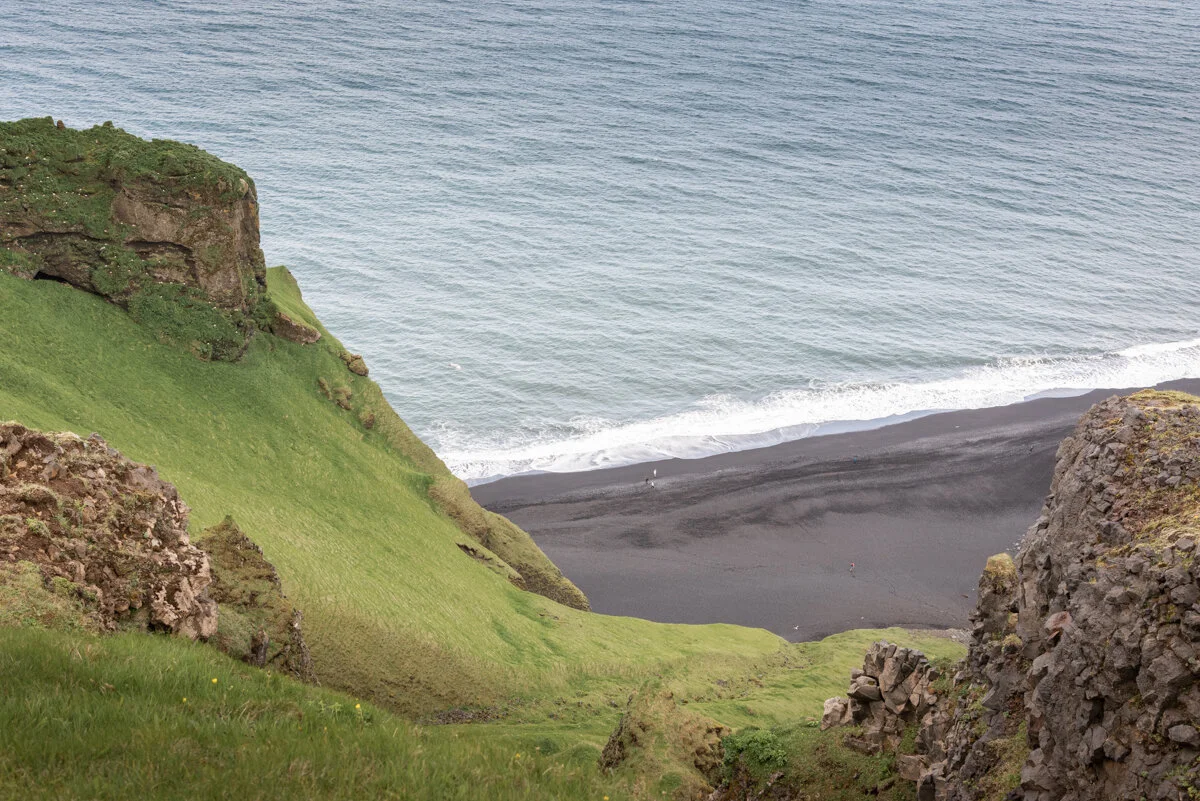 plage de sable noir et océan depuis les falaises rocheuses verdoyantes
