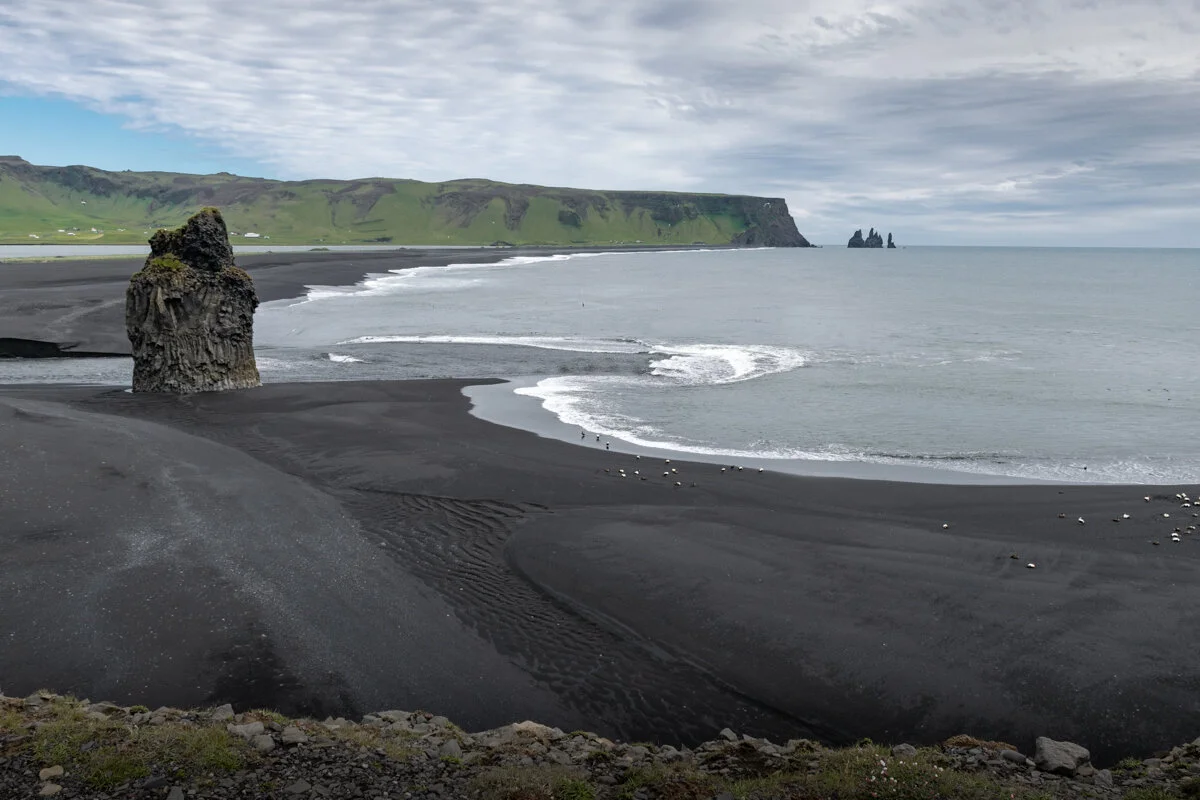 plage de sable noir avec falaise côtière et rocher