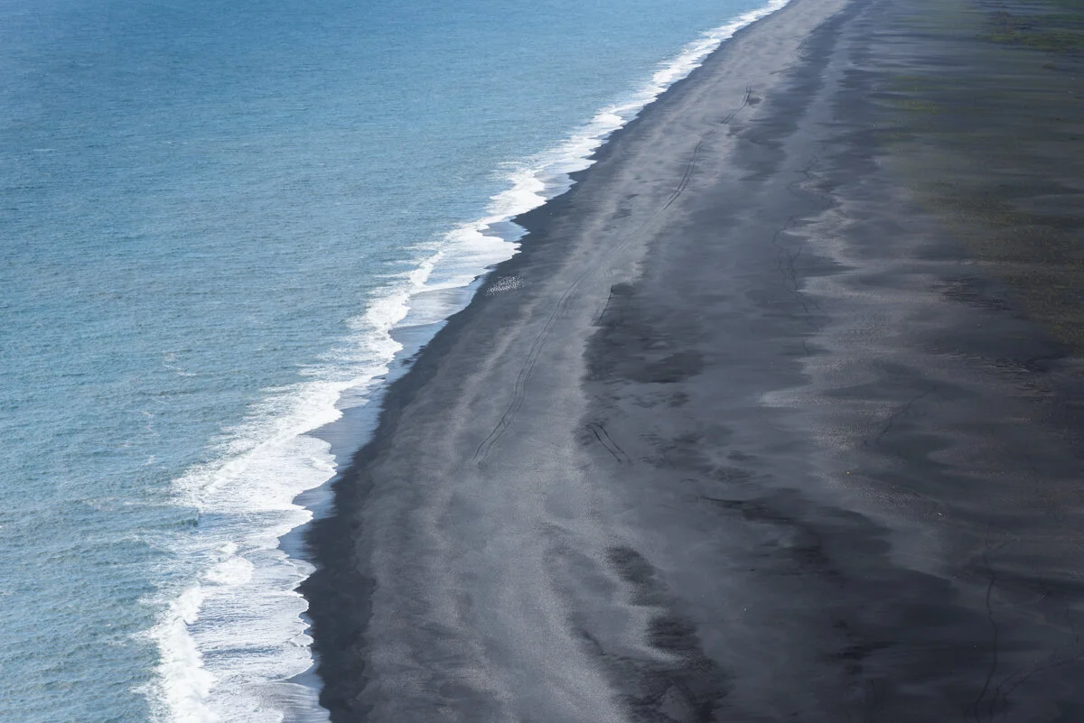 plage de sable noir bordée par l'océan et ses vagues, vue d'en haut