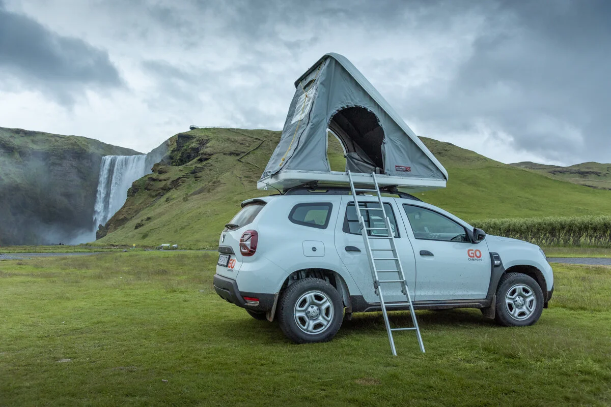 4x4 équipé d'une tente de toit près de Skogafoss que l'on aperçoit en arrière-plan