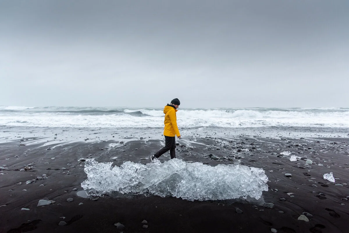 personne sur une plage de sable noir derrière un gros bloc de glace