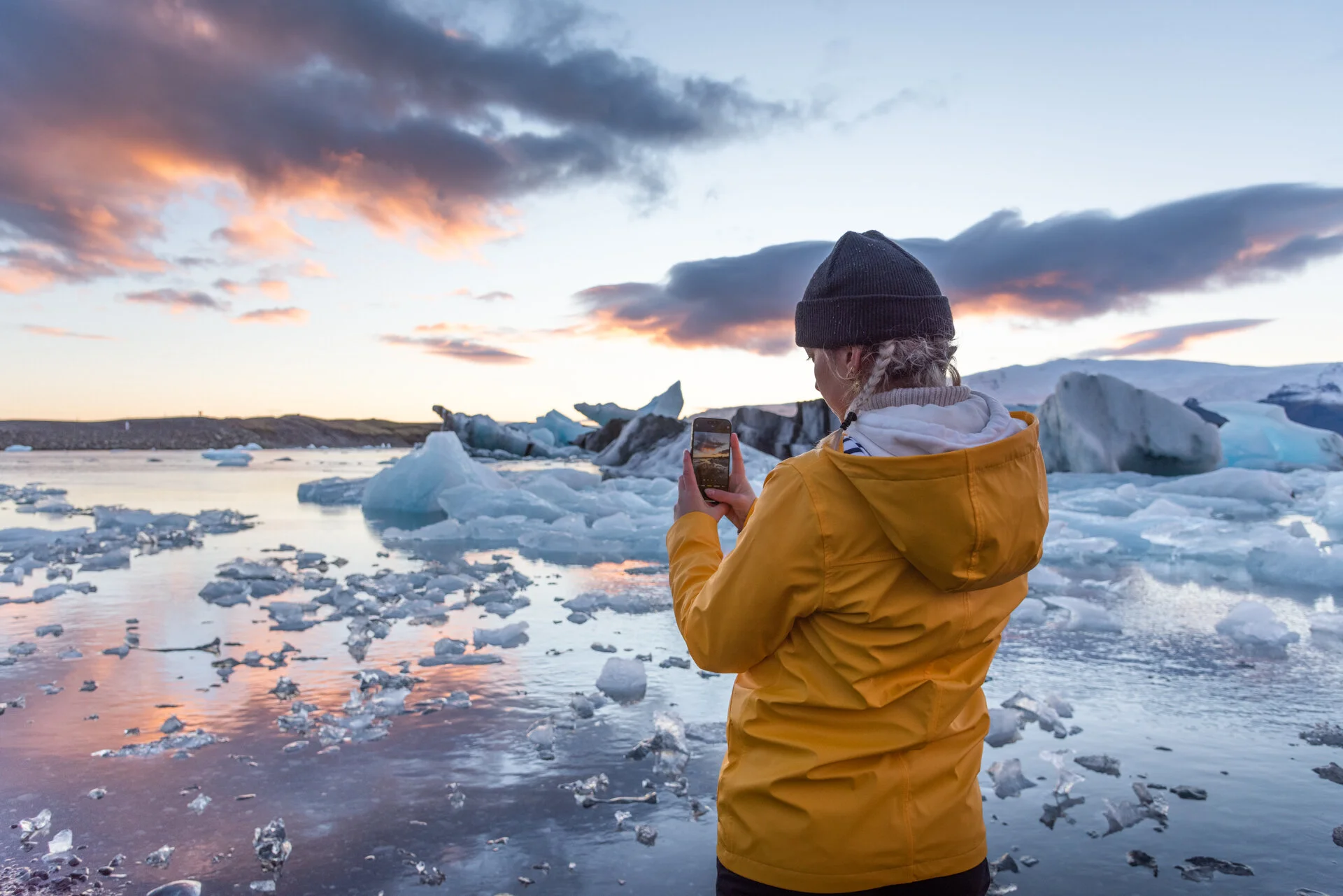 personne en veste jaune photographiant des icebergs à Jökulsárlón au coucher du soleil