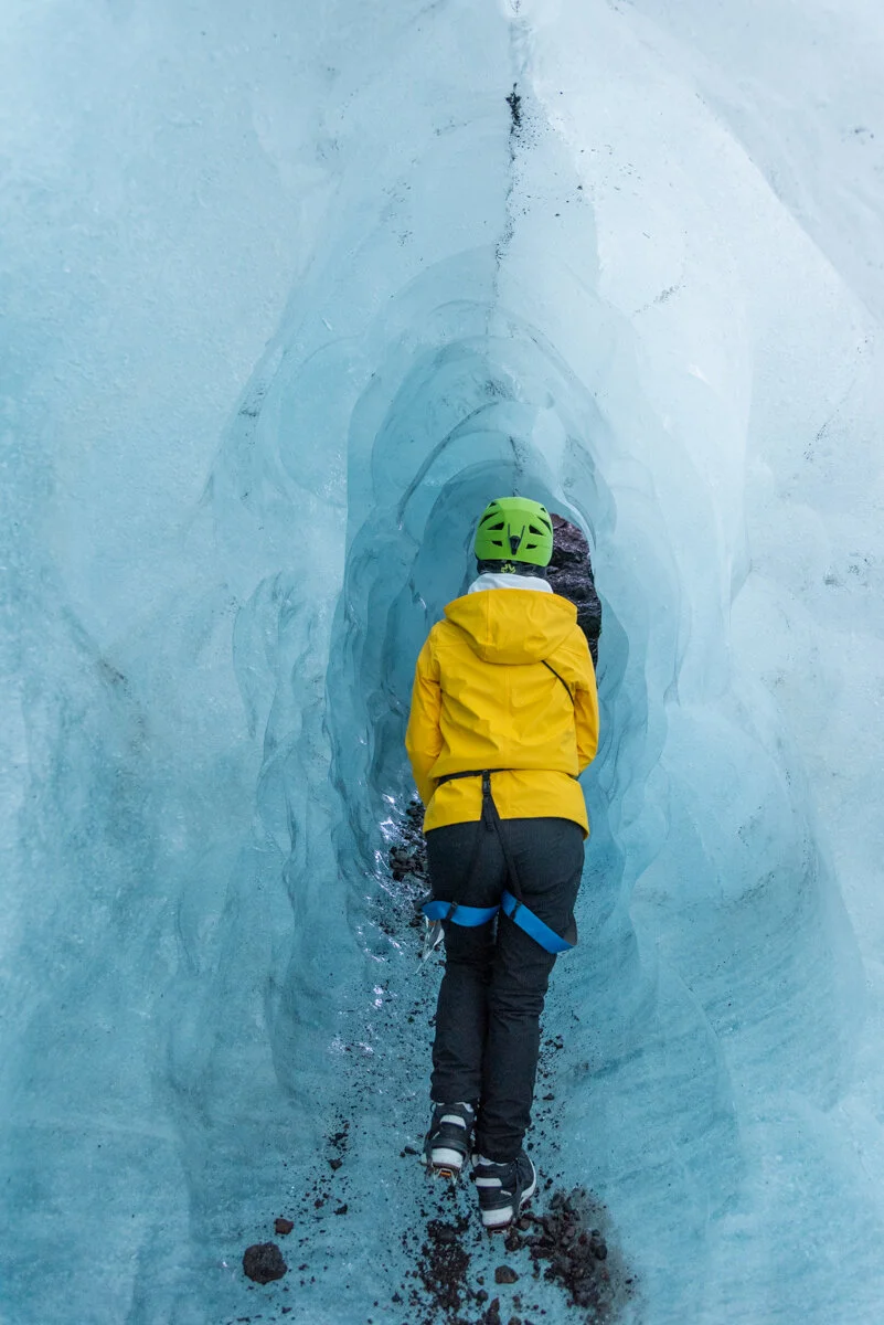 personne équipée qui traverse dans un petit tunnel de glace bleue