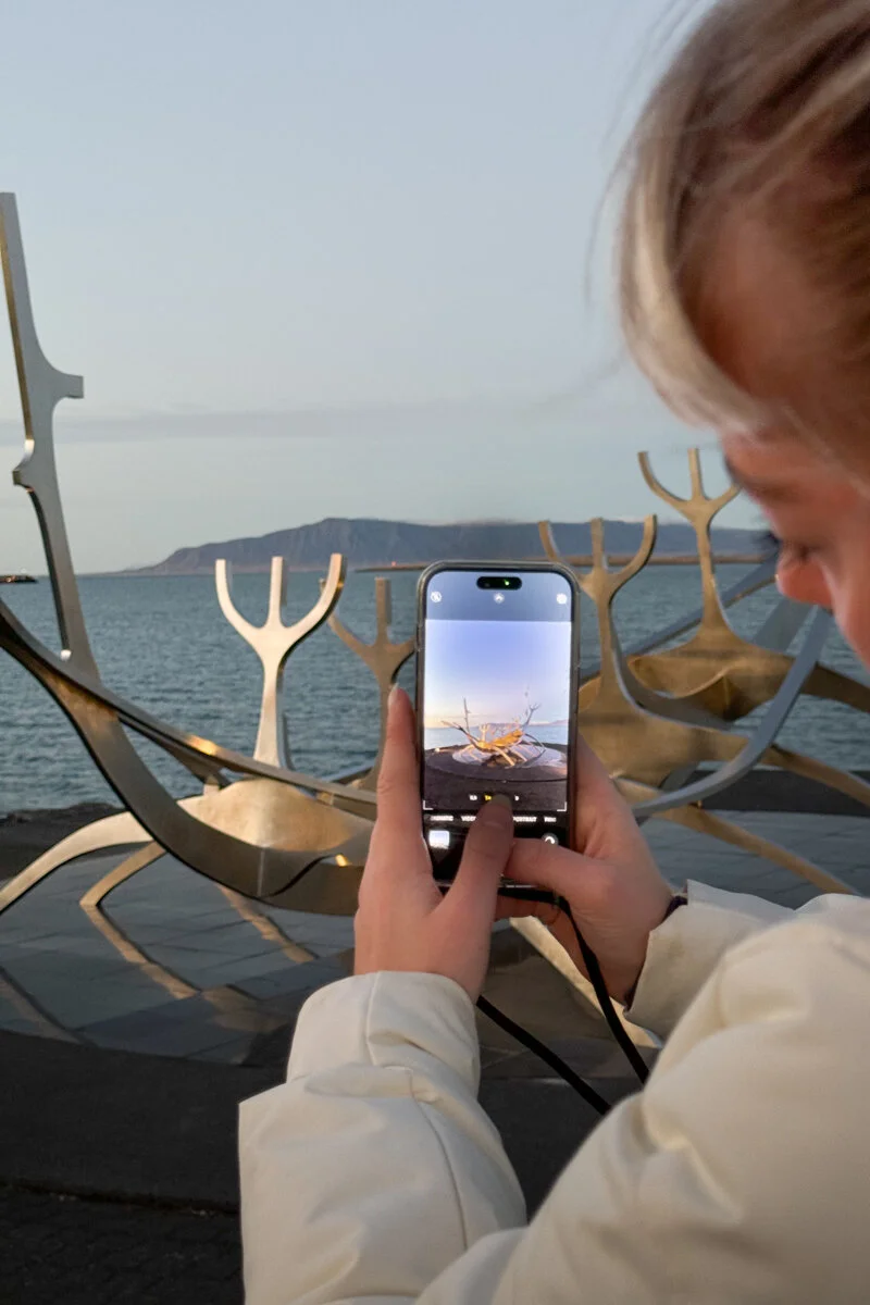 une personne photographie la sculpture de navire viking avec son téléphone