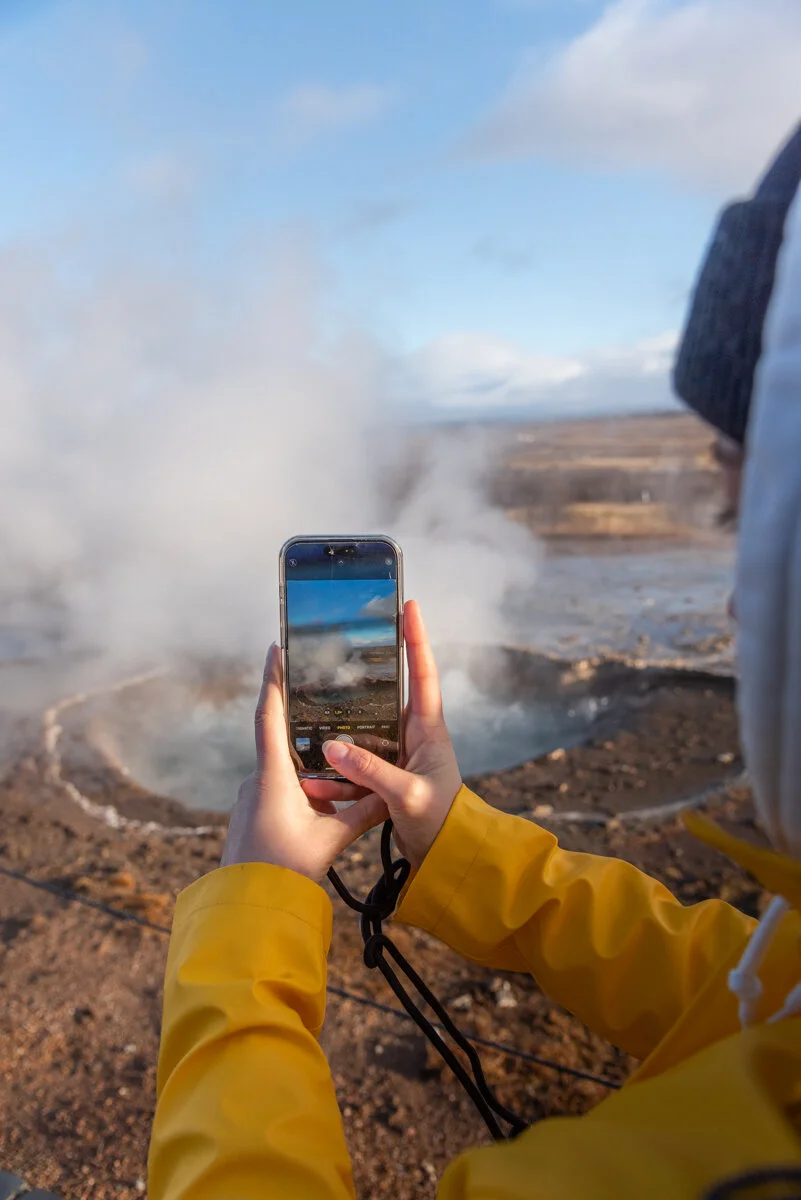 une personne photographie un geyser avec son téléphone