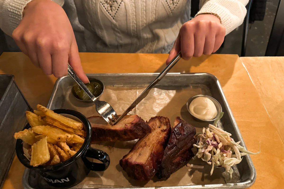 Femme qui tient des couverts pour découper des ribs sur un plateau dans un restaurant, avec des frites