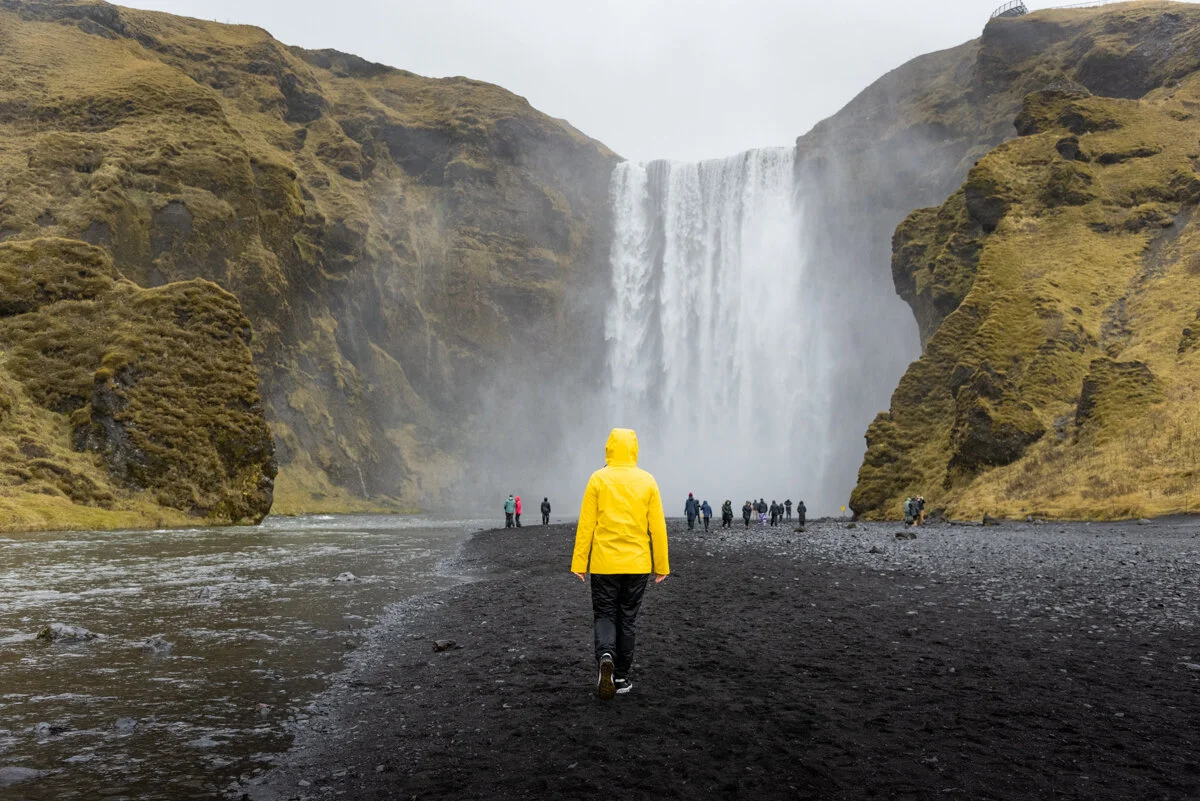 personne en ciré jaune se dirigeant vers Skogafoss