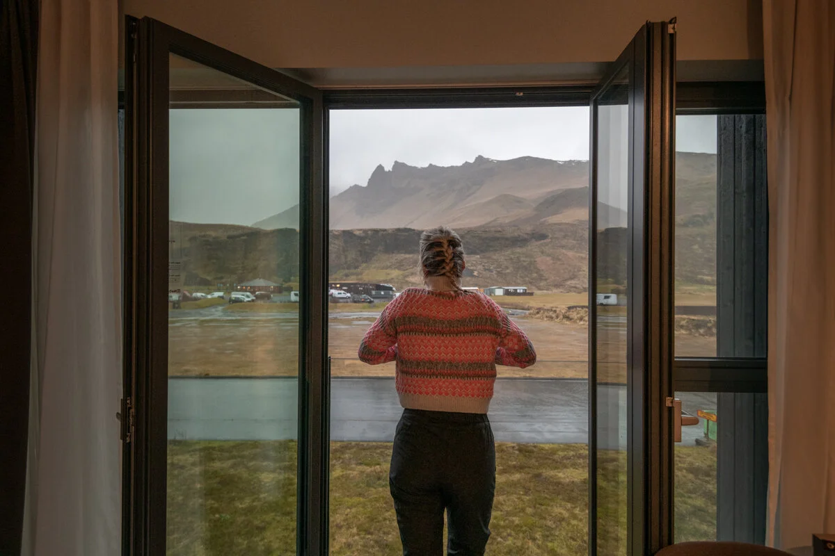 personne vue de dos face à une baie vitrée surplombant un paysage montagneux