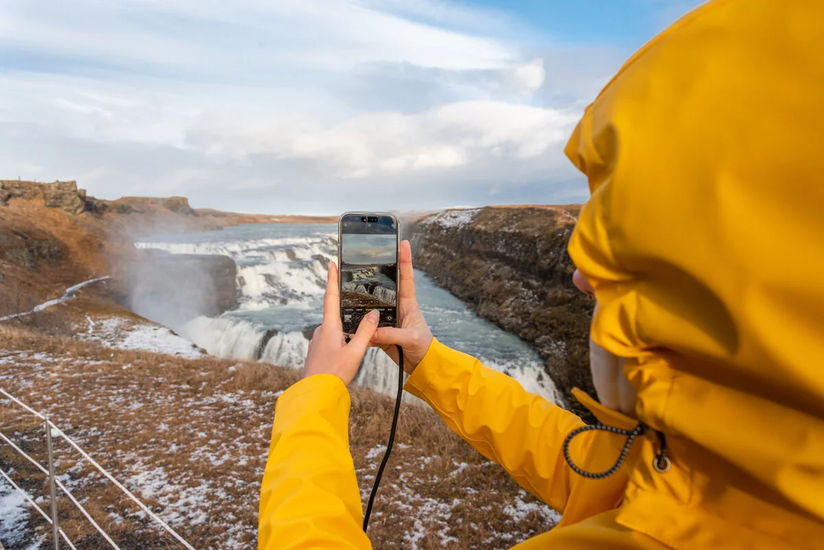 personne en veste jaune photographiant un paysage avec son téléphone