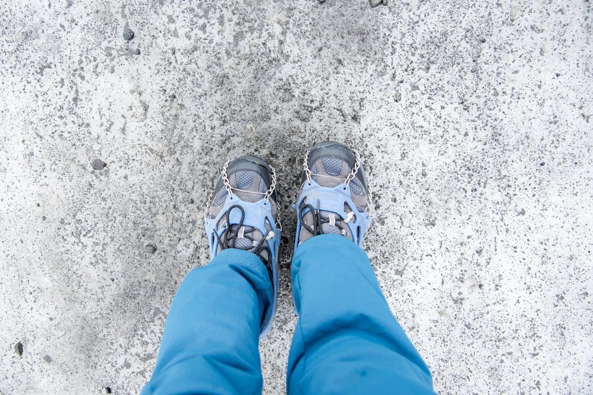 vue de dessus de deux pieds chaussés de crampons sur de la glace