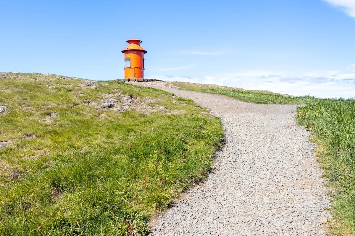 chemin en pense sur une colline herbeuse avec un phare orange au fond
